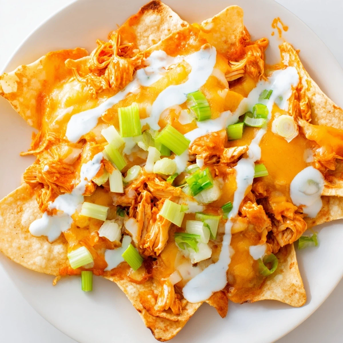 Freshly baked Buffalo Chicken Nachos with a drizzle of cool ranch dressing, served hot on a platter with diced tomatoes.