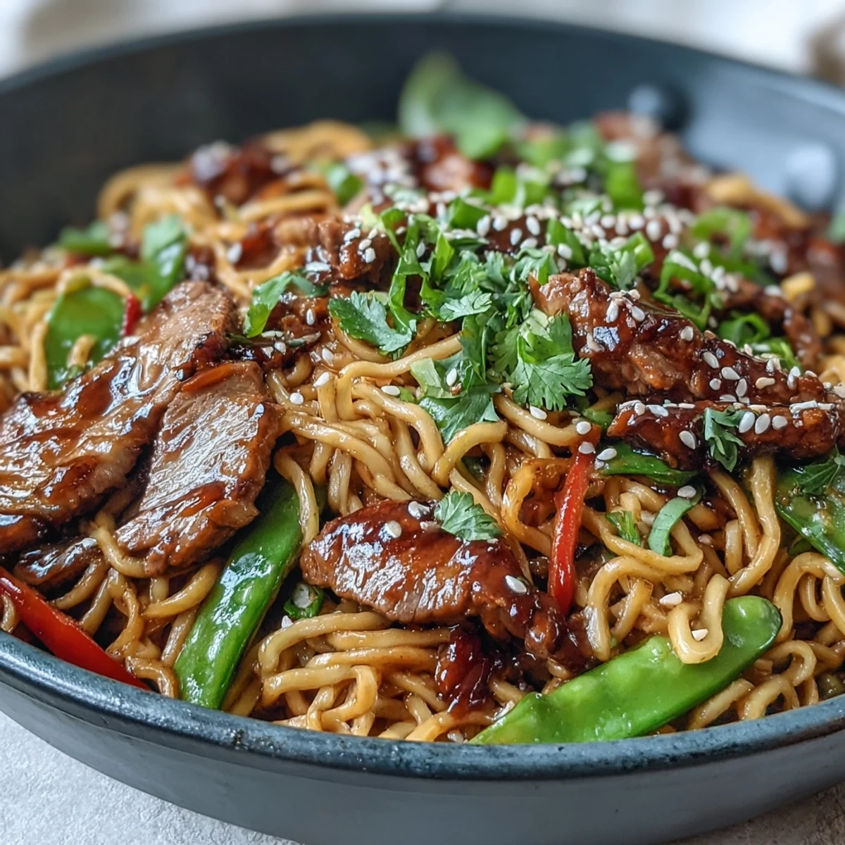 A close-up of colorful Pork Noodle Stir-Fry with julienned carrots and snap peas, steaming on a white plate ready to eat.