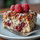 Golden brown Baked Oatmeal with Raspberry and Coconut drizzled with maple syrup in a ceramic dish.  