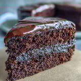 Slice of super-squidgy Easy Chocolate Fudge Cake on a white plate, served with a dollop of whipped cream and fresh raspberries for a festive dessert.