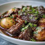 Slow-cooked beef pot roast plated with buttered noodles and parsley garnish, showcasing fall-apart tender meat and a luscious sauce.