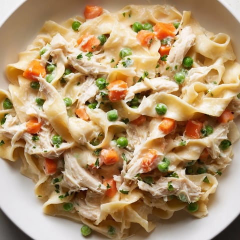 Creamy Spring Chicken Noodle Skillet with tender shredded chicken, sweet peas, and carrots served warm in a skillet.