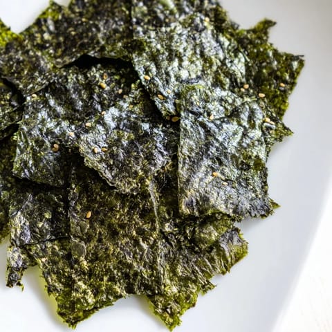 Freshly roasted seaweed chips arranged in a single layer on a baking sheet, showing their crisp, dark green texture.
