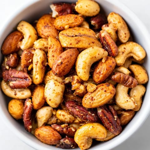 Freshly baked spiced nuts mix cooling on a parchment-lined baking sheet, showcasing clusters with a glossy, sweet-and-savory seasoning.  