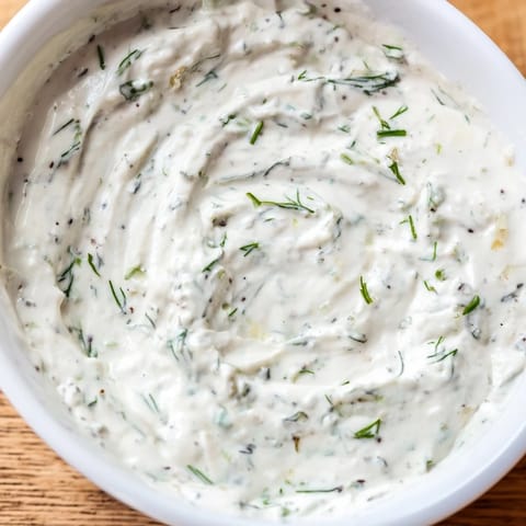 A chilled bowl of Greek Yogurt Herb Dip surrounded by pita chips and fresh veggies for dipping.