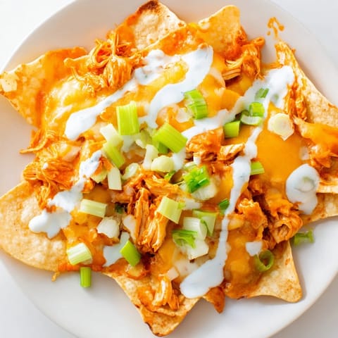 Freshly baked Buffalo Chicken Nachos with a drizzle of cool ranch dressing, served hot on a platter with diced tomatoes.