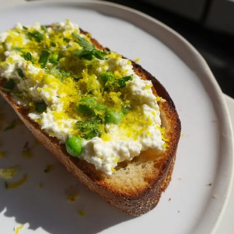 A vibrant open-faced Pea & Mint Ricotta Toast topped with lemon zest and a drizzle of olive oil for brunch.  