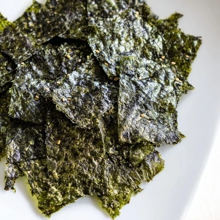 Freshly roasted seaweed chips arranged in a single layer on a baking sheet, showing their crisp, dark green texture.