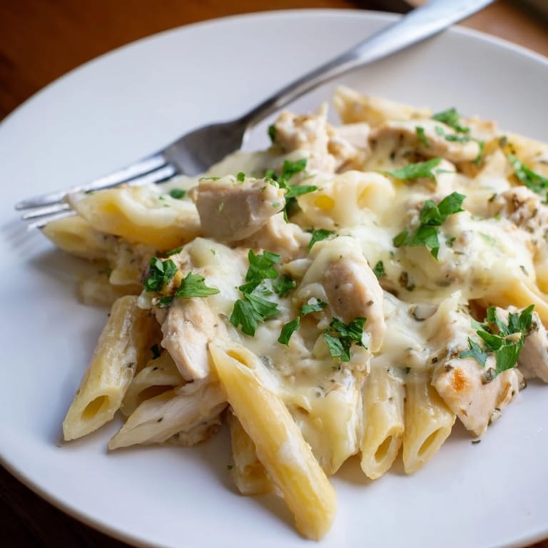 A freshly baked Chicken Alfredo Casserole emerges from the oven, featuring a golden, bubbly mozzarella topping and rich, creamy sauce.