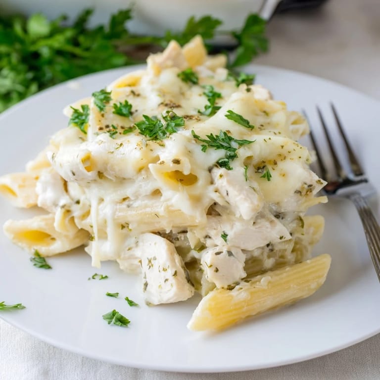 A slice of steaming Chicken Alfredo Casserole reveals layers of tender pasta, shredded chicken, and smooth Alfredo sauce, garnished with fresh parsley.