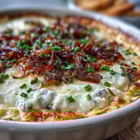 Warm, bubbly Smoked Gouda & Onion Dip topped with fresh chives in a baking dish, served with crispy tortilla chips for dipping.